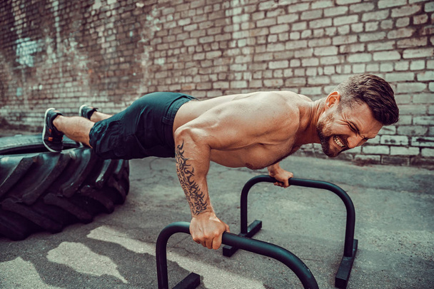Strong sporty happy cheerful positive man doing press exercises holding plank outdoors - Foto, Bild