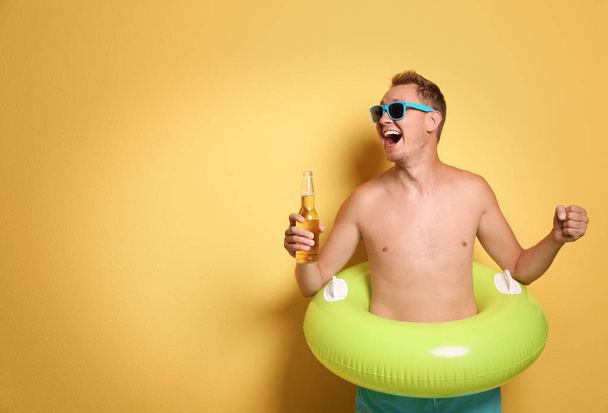 Shirtless man with inflatable ring and bottle of drink on color background - Фото, изображение