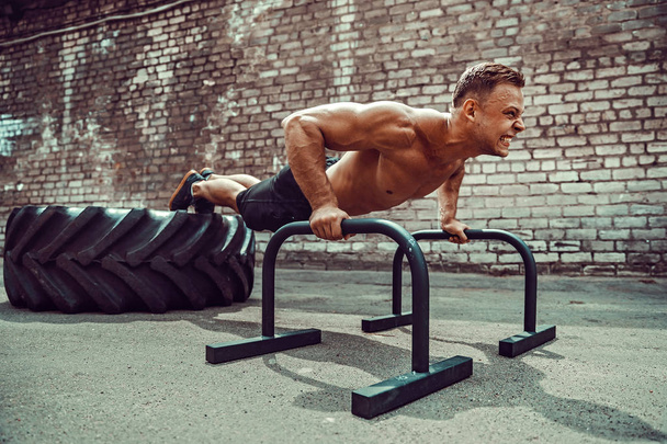 Strong sporty happy cheerful positive man doing press exercises holding plank outdoors - Foto, Imagem