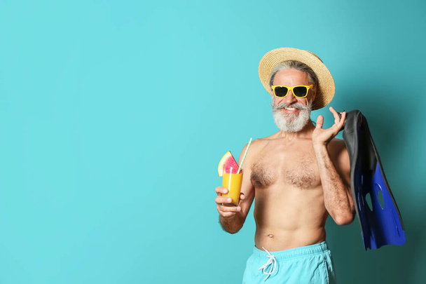 Shirtless man with glass of cocktail and flippers on color background - Valokuva, kuva