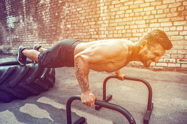 Strong sporty happy cheerful positive man doing press exercises holding plank outdoors - Фото, зображення