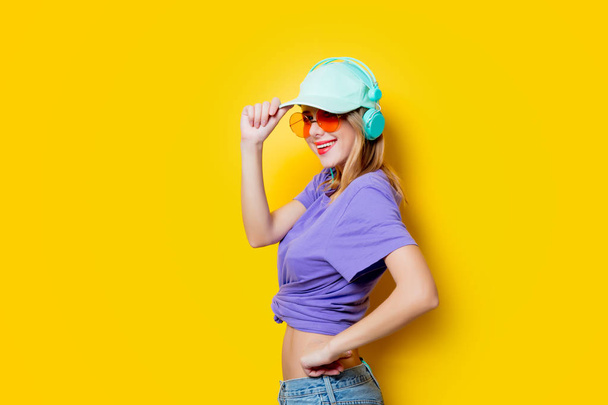 オレンジ眼鏡と黄色の背景の上にヘッドフォンのスタイリッシュな女性。1980 年代スタイルの服 - 写真・画像