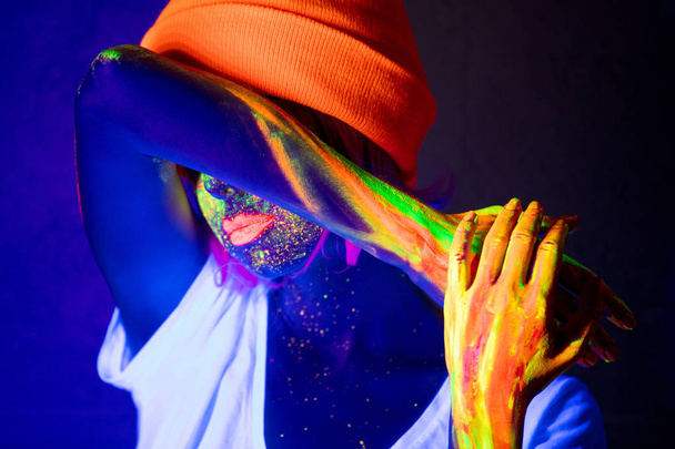 attractive woman in orange hat with fluorescent paint on lips and face - Фото, изображение