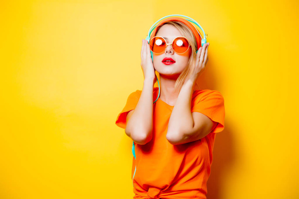 Fiatal stílusos nő a narancsszínű szemüveg és a sárga háttér fejhallgató. 1980-as években stílusosan ruhák - Fotó, kép