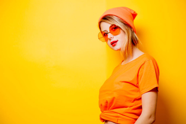 黄色の背景にオレンジ色のメガネでのスタイリッシュな女性。1980 年代スタイルの服 - 写真・画像