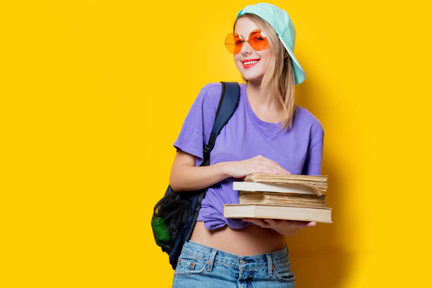Mladý styl studentská dívka s oranžovými brýlemi a knihy na žlutém pozadí. Oblečení ve stylu 80. let - Fotografie, Obrázek