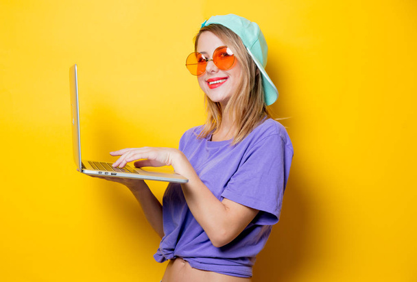 Молода стильна жінка з помаранчевими окулярами та ноутбуком на жовтому тлі. Одяг у стилі 1980-х років
 - Фото, зображення