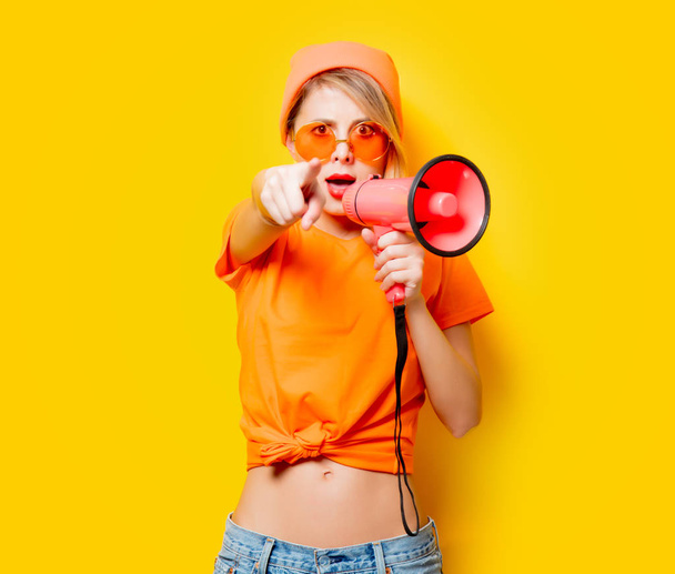 Nuori tyyli tyttö oranssi vaatteita vaaleanpunainen megafoni keltaisella taustalla. Symboloi naisten vastarintaa. Vaatteet 1980-luvun tyyliin
 - Valokuva, kuva
