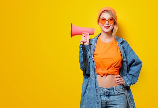 Jeune fille de style en jeans vêtements avec mégaphone rose sur fond jaune. Symbole de la résistance féminine. Vêtements dans le style des années 1980 - Photo, image