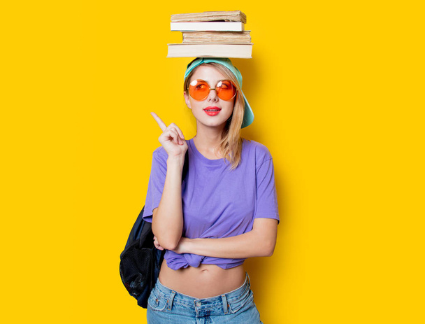黄色の背景にオレンジ色のメガネと本を持つ若いスタイルの学生の女の子.1980年代の服装 - 写真・画像