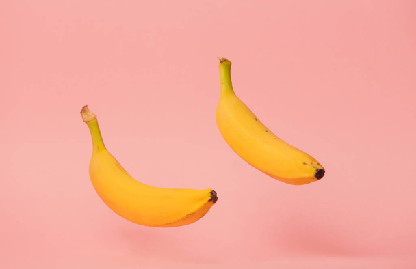 Two yellow bananas levitate in air on pink background. - Photo, Image