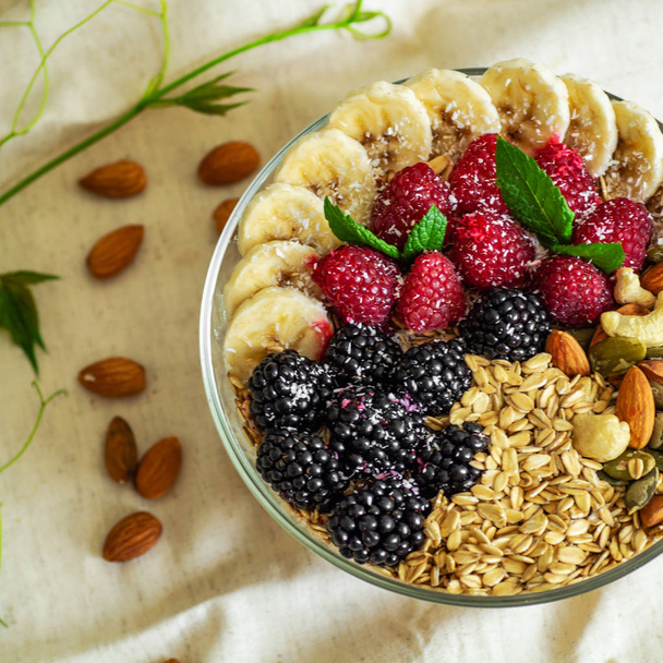 健康的な朝食のボウルを食べる。健康的な食事を有する平板のフルーツ。ラズベリー、バナナ、ナッツ。ダイエット、ベジタリアン食品のコンセプト  - 写真・画像