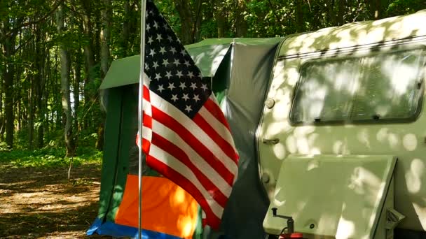  日当たりの良い木、キャラバン、アメリカの国旗が付いているトレーラー。スローモーション - 映像、動画