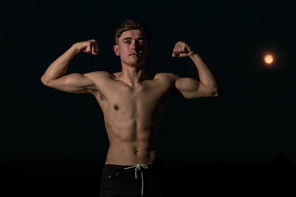 Young adult male flexing his arm muscles at twilight - Foto, immagini