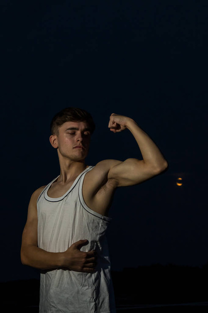 Young male adult outside flexing his arms with the moon - Valokuva, kuva