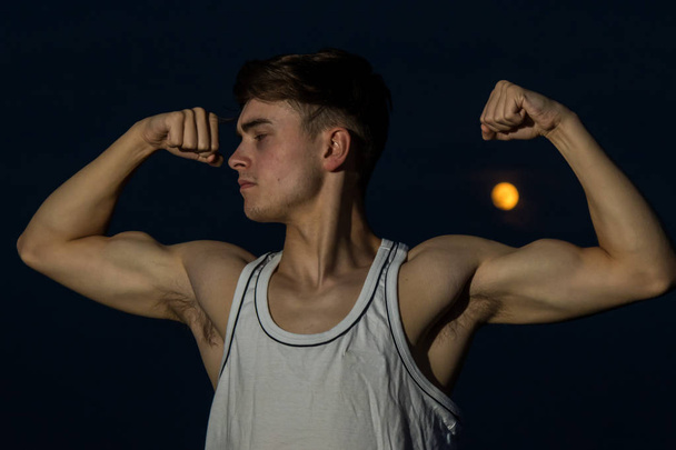 Young male adult outside flexing his arms with the moon - Фото, зображення
