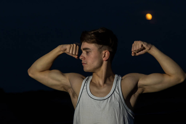 Young male adult outside flexing his arms with the moon - Φωτογραφία, εικόνα
