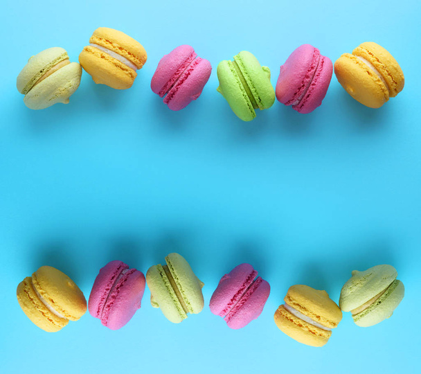 multicolored cakes of almond flour with cream macarons lie in a row on a blue background, copy space in the middle, top view - Photo, Image