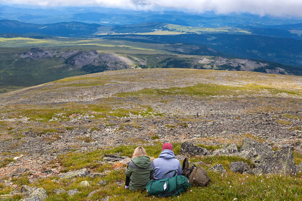 Atmosferyczne moment dla miłośników w górach. Piesze wycieczki, Kobieta i mężczyzna z plecaka jest siedzi na górze montażu i patrząc na piękny krajobraz. Podróż życia i przetrwania koncepcja lusterka - Zdjęcie, obraz