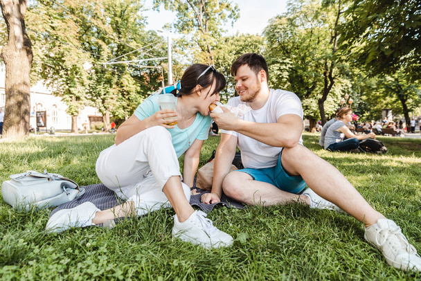 para siedzi na zielonej trawie jedzenie hamburgerów picia koktajl. szeroki Anioł - Zdjęcie, obraz