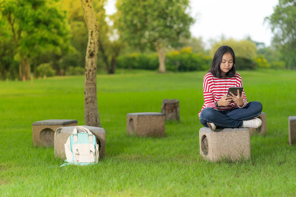 Ασίας φοιτητής κορίτσι χρησιμοποιώντας ένα ψηφιακό tablet στο σχολείο πάρκο σε μια ηλιόλουστη καλοκαιρινή μέρα - Φωτογραφία, εικόνα