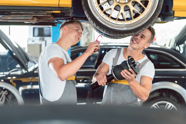Two auto mechanics analyzing the rims of a lifted car - Photo, Image