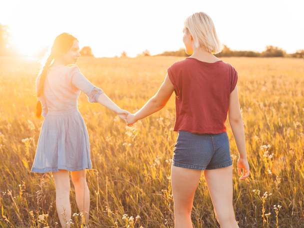 Deux jeunes femmes marchant sur le terrain au coucher du soleil, Meilleures amies
 - Photo, image
