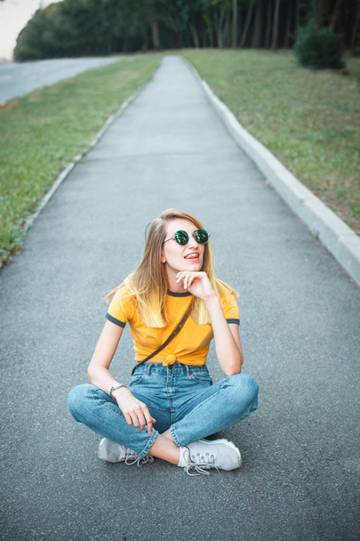 Young woman in sunglasses sitting on road in park - Fotoğraf, Görsel