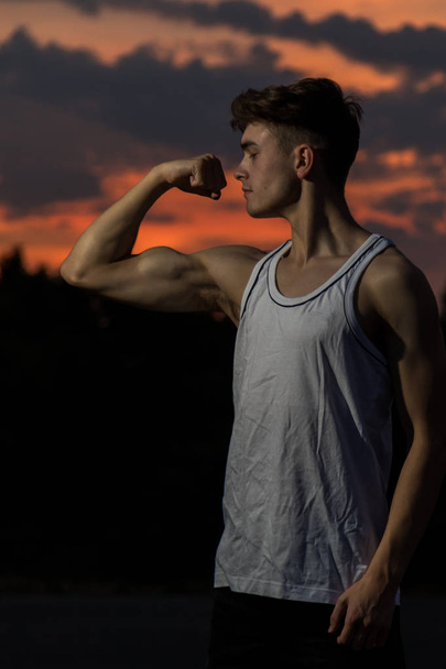 Young male adult flexing his arm  muscles at sunset - Foto, Bild
