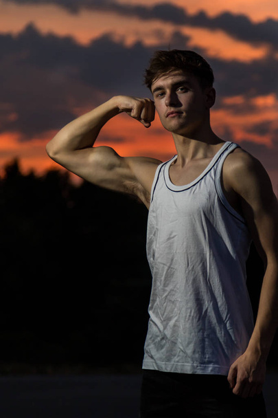 Jovem adulto do sexo masculino flexionando os músculos do braço ao pôr do sol
 - Foto, Imagem