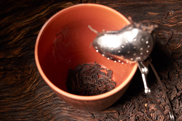 Picture of the tea strainer with dried tea leaves and sticks of cinnamon on darck wooden background - Photo, Image