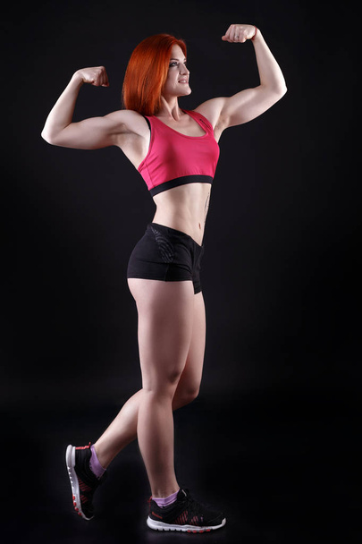 Young strong sexy woman showing her muscles in studio on black background - Photo, Image