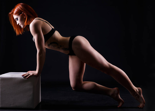Young strong sexy woman showing her muscles in studio on black background - Photo, Image
