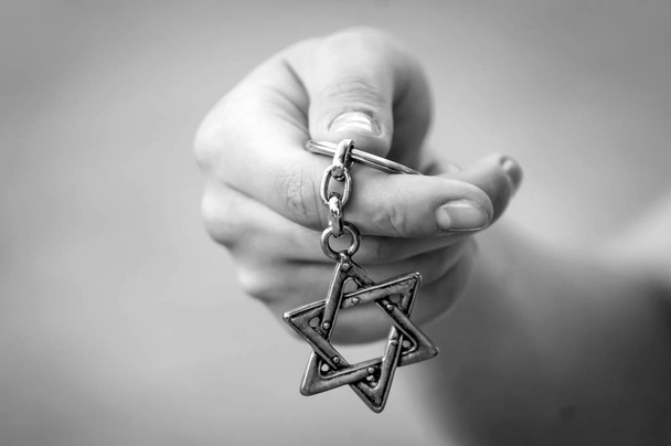 ダビデの星、"Magen David"キー チェーンを持っている若い女性の手。イスラエル共和国の州、ユダヤ教、シオン主義または反ユダヤ主義コンセプト イメージで。ホロコーストの記念日。黒と白のイメージ. - 写真・画像
