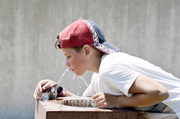 Кавказький11-річний хлопчик у бейсбольній шапці п'є воду з жагою від плямистості в спекотну літню погоду
 - Фото, зображення