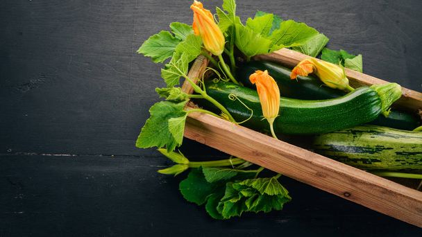 Green zucchini in a wooden box. Fresh vegetables. On a black wooden background. Top view. Copy space. - Foto, Imagen