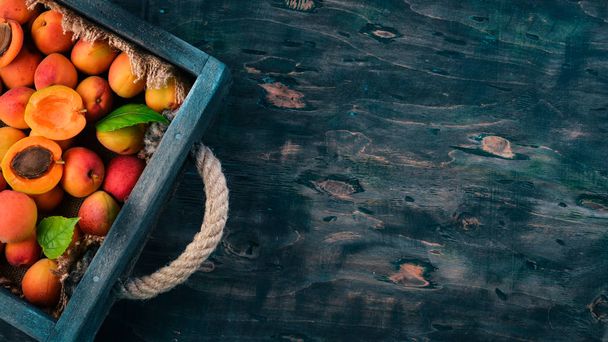Apricots in a wooden box. Fresh fruits. On a black wooden background. Top view. Free space for your text. - Foto, Imagem