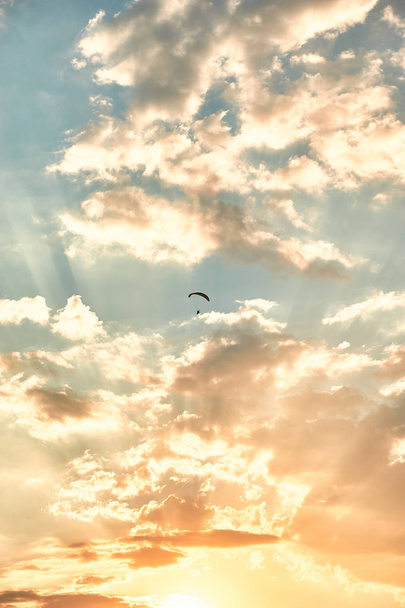 une petite silhouette de parapente au milieu des nuages à la lumière du soleil couchant
 - Photo, image