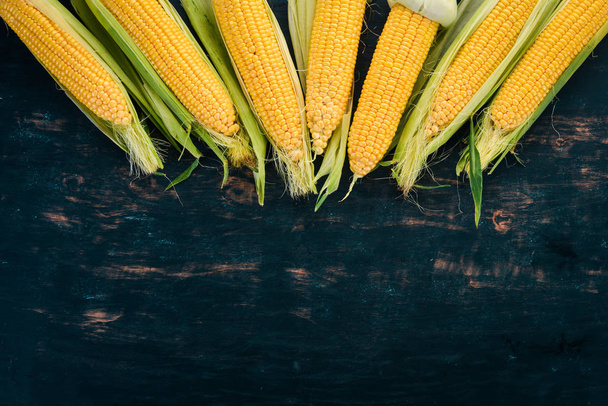 Fresh yellow corn on a black wooden table. Vegetables. Top view. Copy space. - Фото, зображення