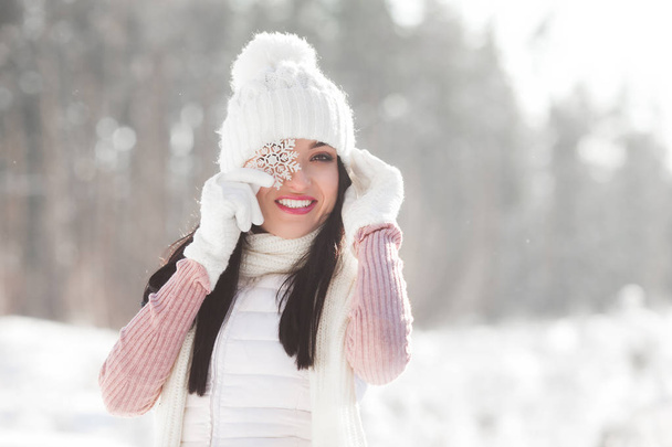 Smiling young woman covering her eye with snowflake. Cheerful preety girl at winter background. - Foto, Imagem