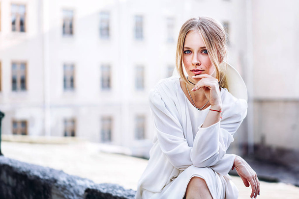 Portrait of woman in white vintage dress sitting outdoor on blurred house background. - Φωτογραφία, εικόνα