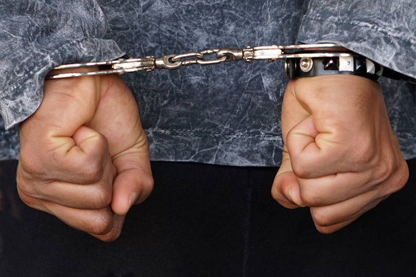 Close-up. Gearresteerde man geboeid handen aan de achterkant geïsoleerd op een grijze achtergrond. Gevangene of gearresteerd terrorist, close-up van handen in handboeien. - Foto, afbeelding