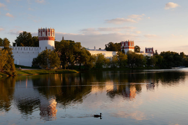 The walls and towers of the Novodevichy monastery in Moscow are reflected in the water in the summer evening sunset - Foto, Bild