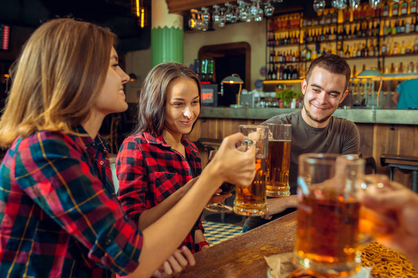 people, leisure, friendship and communication concept - happy friends drinking beer, talking and clinking glasses at bar or pub - Фото, зображення