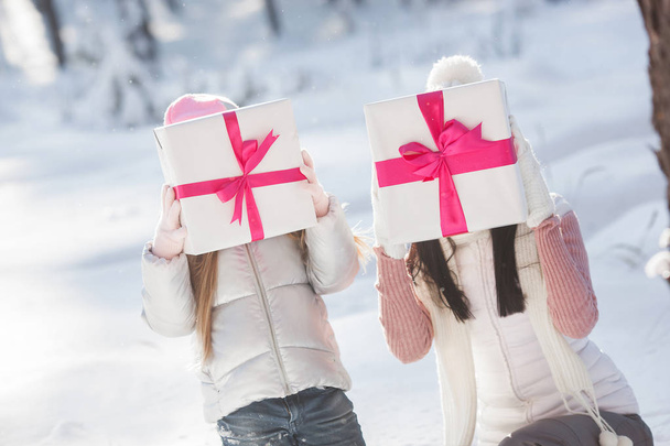 Молодая красивая мать и ее маленькая девочка веселятся на открытом воздухе зимой. Веселый ребенок и ее красивая мама играют со снегом на природе. Подарки для семьи на Рождество. Подарок на их лицах
 - Фото, изображение