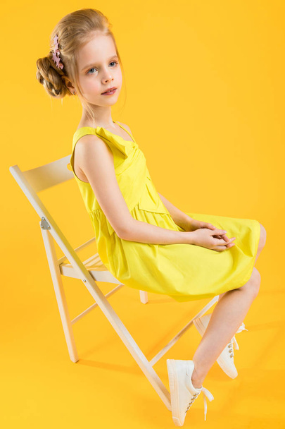A girl is sitting on a white chair on a yellow background. - Foto, Imagem