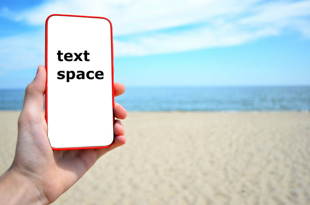 Hand holds the phone on the beach background, space for text - 写真・画像