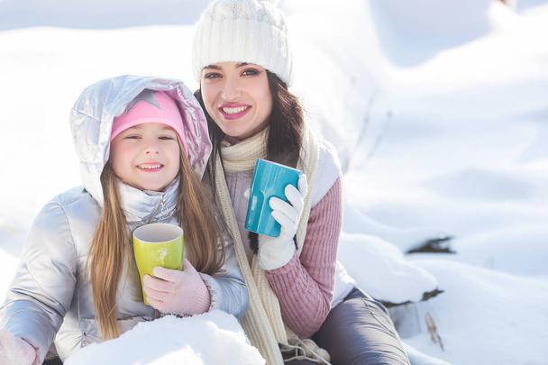 Mother and her daughter having fun outdoors in winter time. Pretty family drinking tea and cocoa - Photo, Image