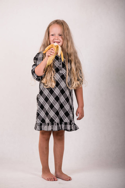 schöne süße kleine Mädchen essen leckere gesunde Banane auf weißem Hintergrund - Foto, Bild
