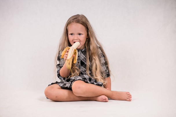 白い背景でおいしい健康的なバナナを食べて美しいかわいい女の子 - 写真・画像